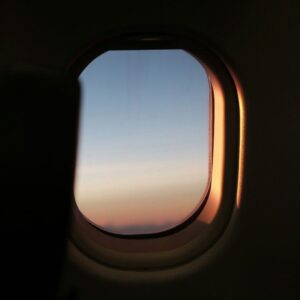 View through an aircraft cabin window at dusk, the rim lit by low sun