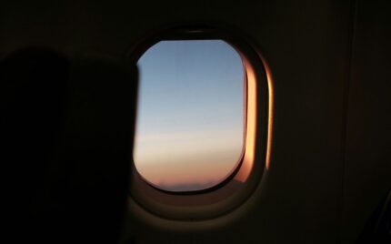 View through an aircraft cabin window at dusk, the rim lit by low sun