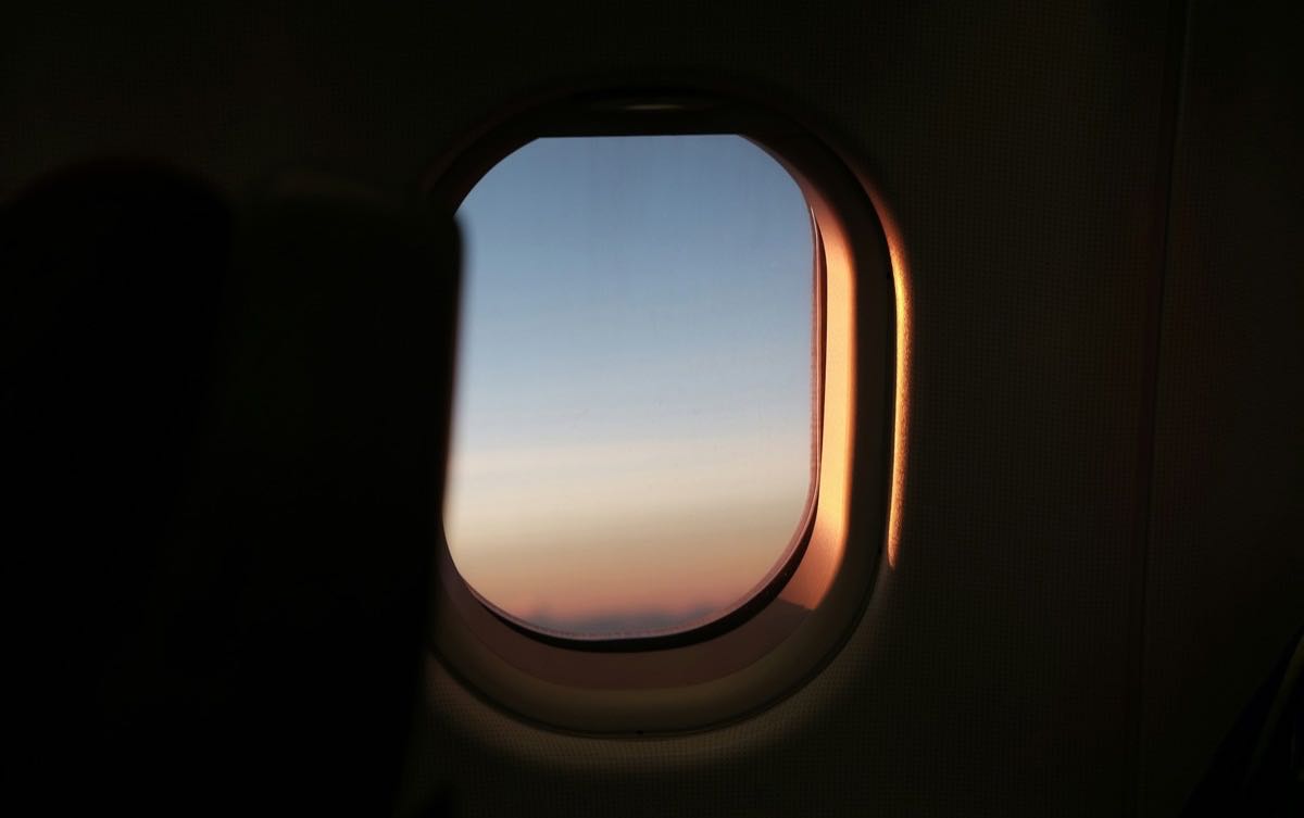 View through an aircraft cabin window at dusk, the rim lit by low sun