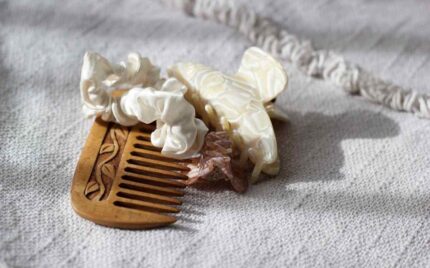 A wooden comb, a cream scrunchie and a pearl-toned claw clip resting on soft woven fabric